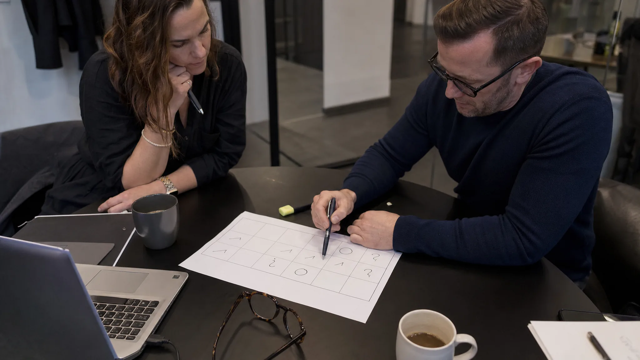 Deux collègues annotent au stylo une grille de comparaison imprimée sur une table de réunion